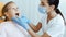 Young female doctor in white coat, protective mask and gloves examines child teeth