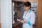 A young female doctor in white uniform is standing in a room for medical staff near a cabinet with pills