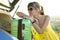 Young female driver having rest leaning on a green suitcase near her car in summer nature. Travel and vacations concept