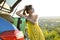 Young female driver having rest leaning on a suitcase in her car in summer field. Travel and vacations concept