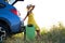 Young female driver having rest sitting on a green suitcase near her car in summer nature. Travel and vacations concept