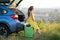 Young female driver having rest sitting on a suitcase near her car in summer field. Travel and vacations concept