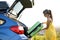 Young female driver putting green suitcase inside her car trunk. Travel and vacations concept