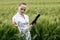 Young female ecologist scientist in goggles standing in green field and working on glass transparent screen