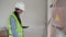 A young female electrician works with a tablet standing near an industrial fuse board cabinet and wiring