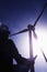 Young female engineer holding open blueprints and checking wind turbines on site, silhouette, low angle view