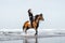 young female equestrian riding horse in wavy water