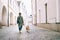 Young female fancy-dressed using a face mask as a coronavirus spreading prevention walking with her beagle dog on deserted old