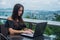 Young female freelancer dressed in black working on a project laptop computer while sitting at rooftop cafe terrace