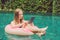 Young female freelancer sitting with a tablet in an inflatable circle in the pool. Busy at holidays. Distant work