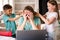 A young female freelancer works from home remotely using a laptop. Women children do her hair and interfere with work