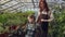 Young female gardener in apron and her cute daughter are dancing in greenhouse having fun. Happy family, gardening