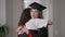 Young female graduate in gown and hat hugging woman with dissatisfied irritated facial expression. Caucasian