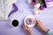 Young female hands holding plate with sweet donut near cup of coffee, bouquet of purple and white tulips, hanger with clothes.