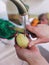 Young female hands peel potatoes with a knife over a sink