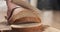 Young female hands slicing rye wheat rustic bread on cutting board