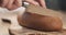 Young female hands slicing rye wheat rustic bread on cutting board