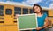 Young Female Hispanic Student with Blank Chalkboard Near School Bus