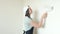 Young female house painter paints a white wall with a roller.