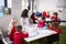 Young female infant school teacher sitting at a table in a classroom with her pupils