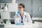 A young female internist is sitting at a desk in her spacious, bright office, wearing gloves and a medical gown