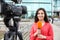 Young female journalist with microphone working on street