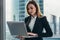 Young female lawyer working in her luxurious office holding a laptop standing against panoramic window with a view on