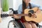 Young female musician in wheelchair playing guitar at home
