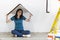 Young female in new empty room with carton cardboard over her head making as roof. Beautiful attractive female sitting on floor