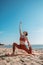 Young female in orange top and leggins practising Crescent Moon Pose Anjaneyasana Variation  on a beach in the morning