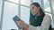 Young female passenger at the airport, using her tablet computer while waiting for her flight, smiling, sunnu day