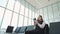 Young female passenger at the airport, using her tablet computer while waiting for her flight, smiling, sunnu day