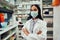 Young female pharmacist in labcoat and covid-19 face protection mask working in chemist