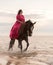 Young female in a pink dress joyfully riding her horse through a shallow body of water