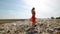 Young female pollution activist in red dress standing at huge trash dump