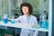 Young female researcher in eyeglasses and lab coat taking test tube from shelf