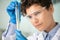 Young female researcher in gloves, eyeglasses and whitecoat studying substance