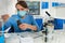 Young female scientist in uniform wearing a mask weighs powder o