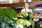 Young female seller in apron offering fresh greens and letuce