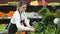 Young female seller in gloves working fresh greens and letuce on the market