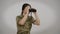 Young female soldier with binoculars looking away posing at grey background. Medium shot portrait of concentrated