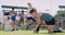 A young female sports person kneeling tying her shoelaces while on a field with teammates in the background. Hockey