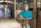 Young female stable keeper carrying horse saddle and harness