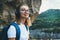 Young female student looks up in hipster glasses and wireless headphones enjoys nature in the mountains while Hiking walk, freedom