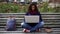 Young female student sitting on bench with laptop outdoors concentrated on study