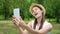 Young female student in white shirt sitting on grass on college campus doing selfie on mobile phone