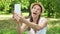 Young female student in white shirt sitting on grass on college campus doing selfie on mobile phone