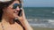 Young female in sunglasses answering phone call on beach, smiling, talking