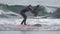 Young female surfer athlete wearing in black wetsuit cruising along breaking wave in Pacific Ocean. Slow motion shot