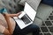 Young female tech user relaxing on sofa holding laptop computer and smart phone mock up with  blank screen.